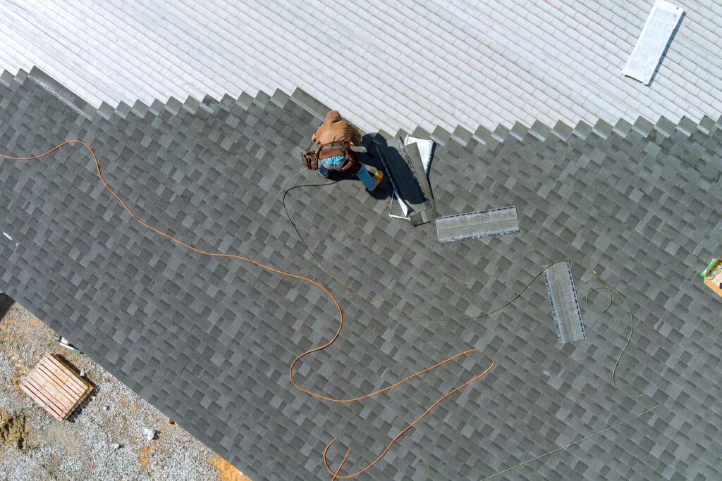 A drone shot of a worker replacing shingles on a roof. 