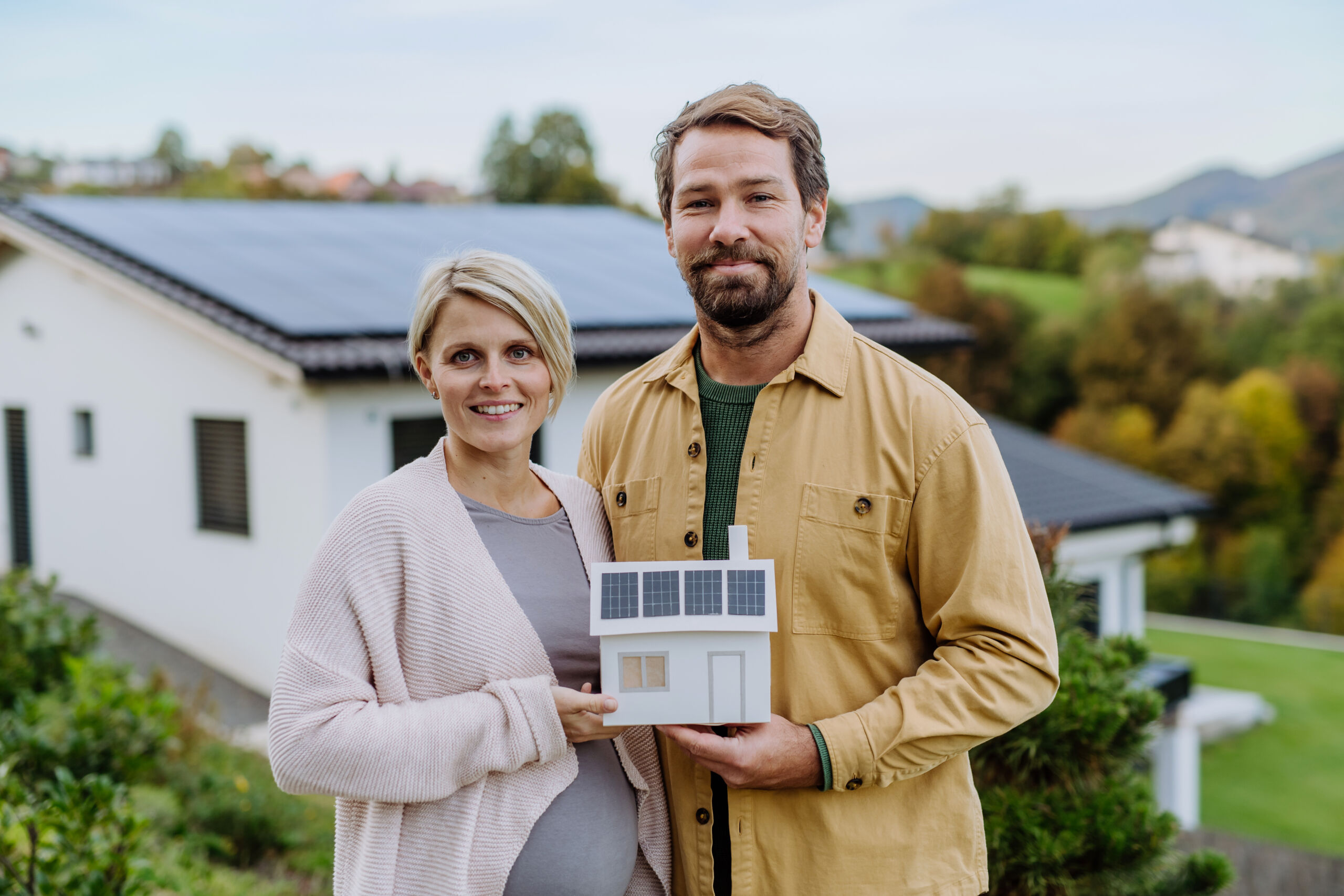 An image of a happy couple in front of their solar home, enjoying how their solar panels fix rates for their bill. 