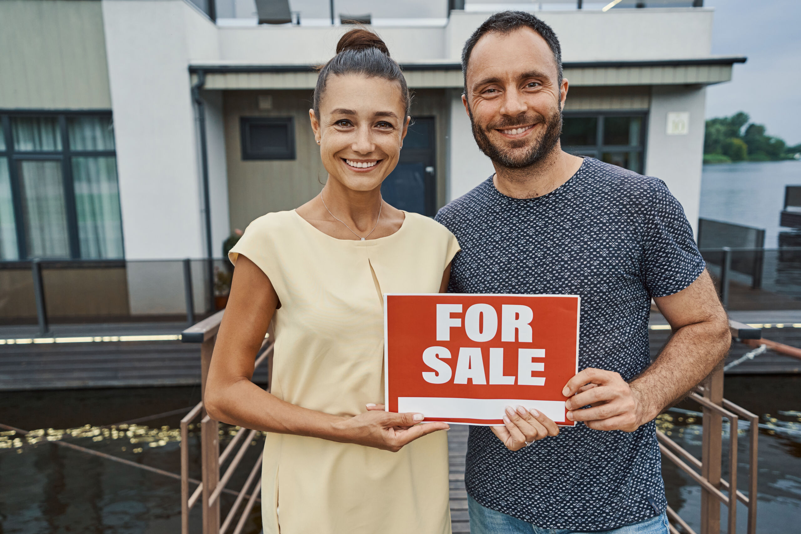 An image of a married couple holding up a for sale sign in front of their solar home for more value. 