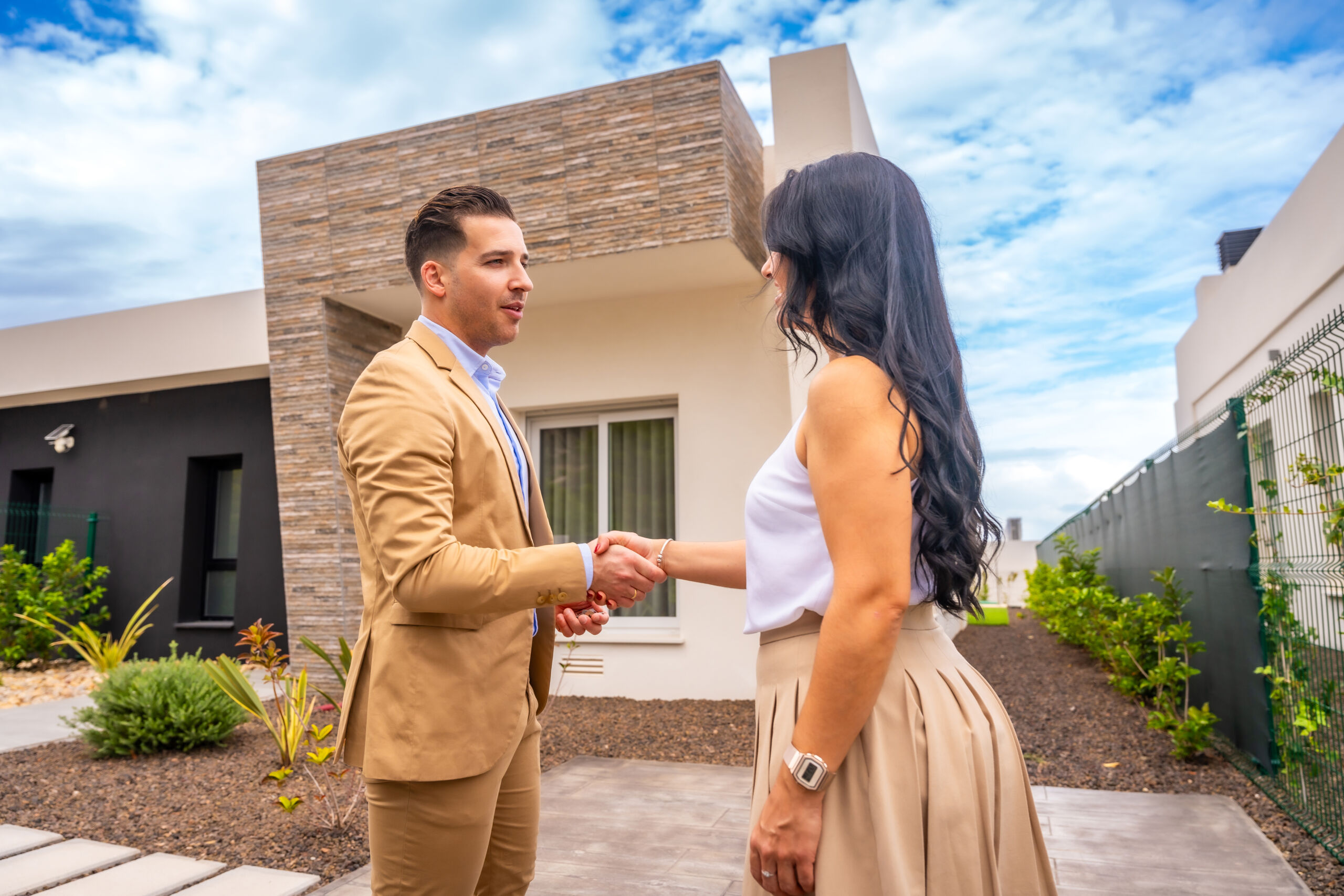 An image of a young woman shaking hands with a realtor. She has just purchased this solar home for more money because it will save her long term.