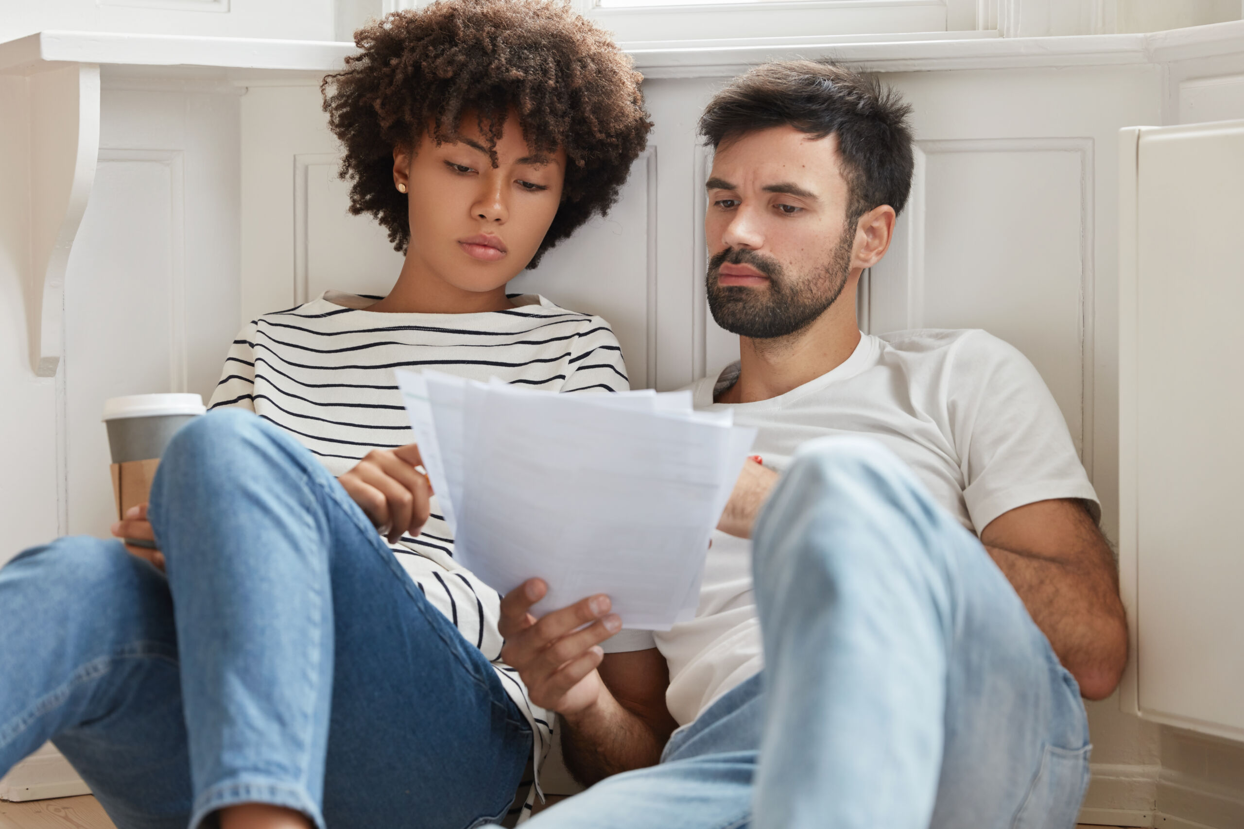 A young, married couple leans against the wall in their home. They are looking at their insurance rising insurance costs.